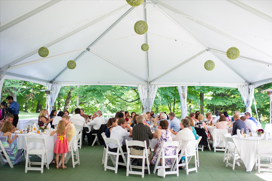 wedding guests sit at round tables under tent